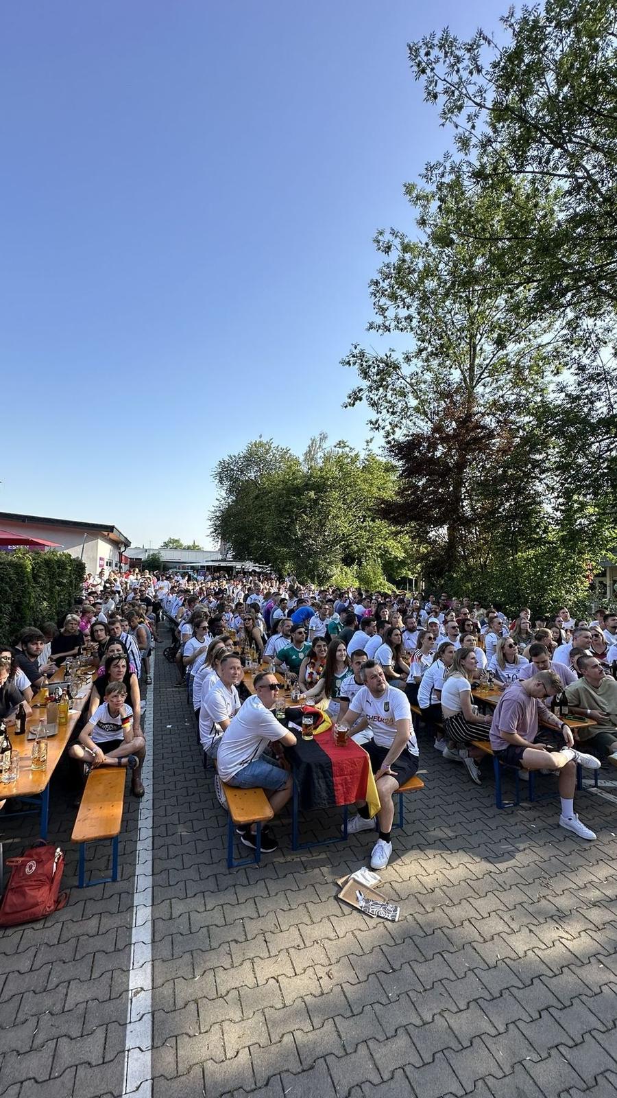 Gin Tonic mit Rosmarin im GINSTR-Glas vor blauem Himmel, dahinter unscharf die Leinwand